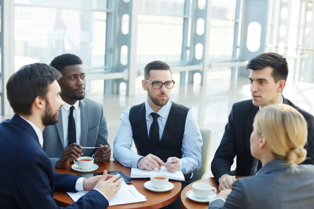 Has Kuflink Changed during covid (1) A group of business people gathered around a table discussing contracts while sipping on hot beverages