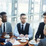 A group of business people gathered around a table discussing contracts while sipping on hot beverages